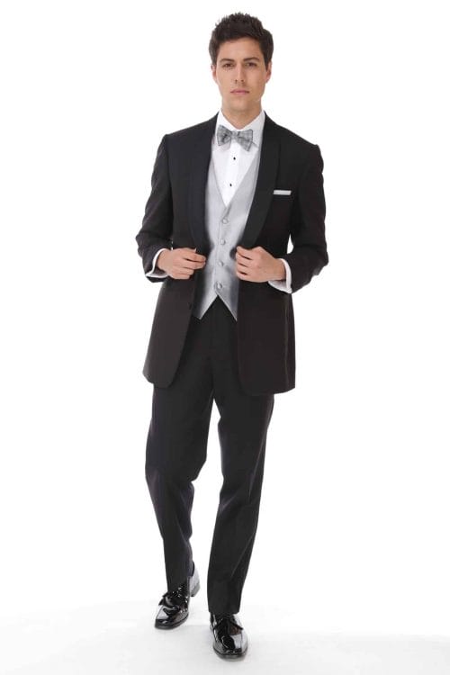 A man in a black tuxedo posing for a photo at a suit rental shop.