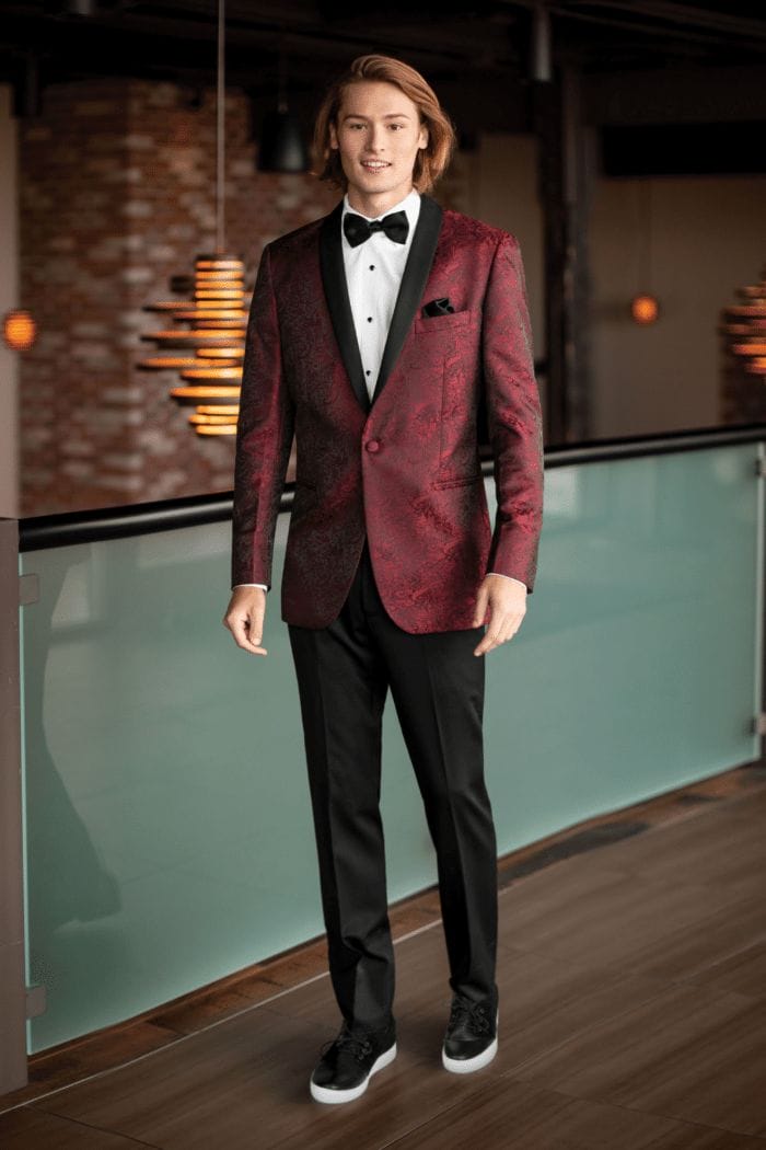 A man in a red tuxedo standing in a hallway, showcasing the perfect suit rental.