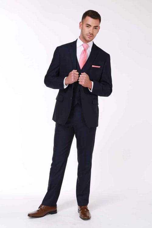 A man is posing in a Renoir Navy Suit with a pink tie available for suit rental.