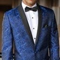 A man in a blue tuxedo poses for a photo at a suit rental shop.