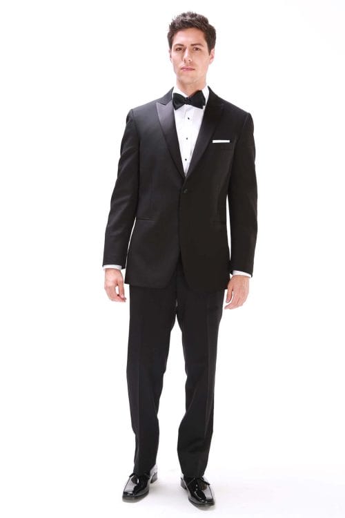 A man in a black After Six Milano tuxedo, available for tuxedo rental or suit rental, standing in front of a white background.
