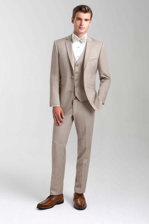 A man in a tan Allure Charcoal tuxedo is posing for a photo, showcasing the elegance of tuxedo rental.