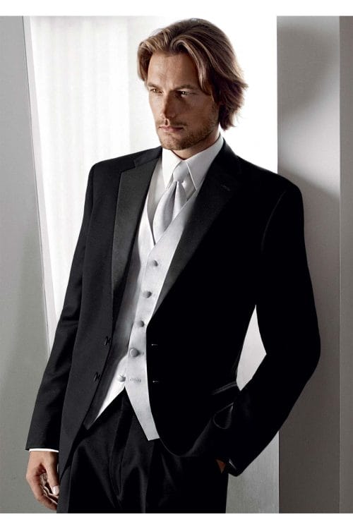 A man in an Allure Charcoal tuxedo leaning against a wall, showcasing the elegance of tuxedo rental.