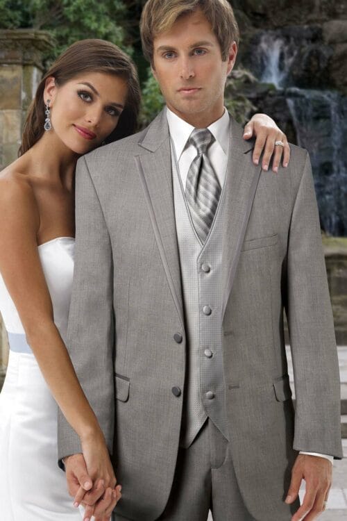 A man and woman, both dressed in their finest Allure Charcoal suits rented for the occasion, are posing for a picture in front of a breathtaking waterfall.