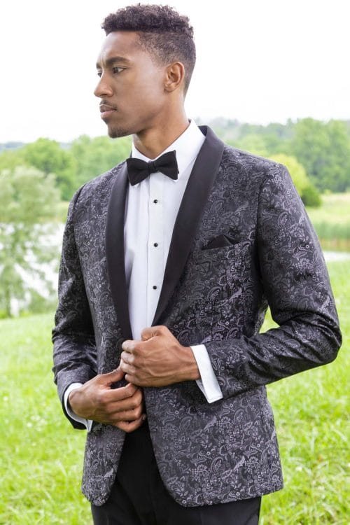 A man in an Allure Charcoal tuxedo standing in a field, showcasing the elegance of tuxedo rental.