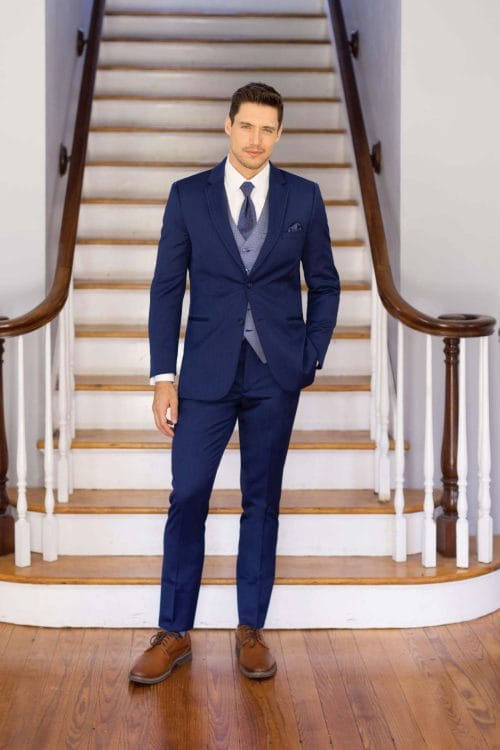 A man in a blue suit standing on a staircase, exuding the elegance of Allure Charcoal suit rental.