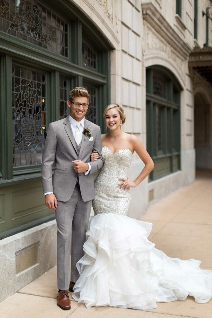 A groom posing in front of the Allure Heather Grey building.