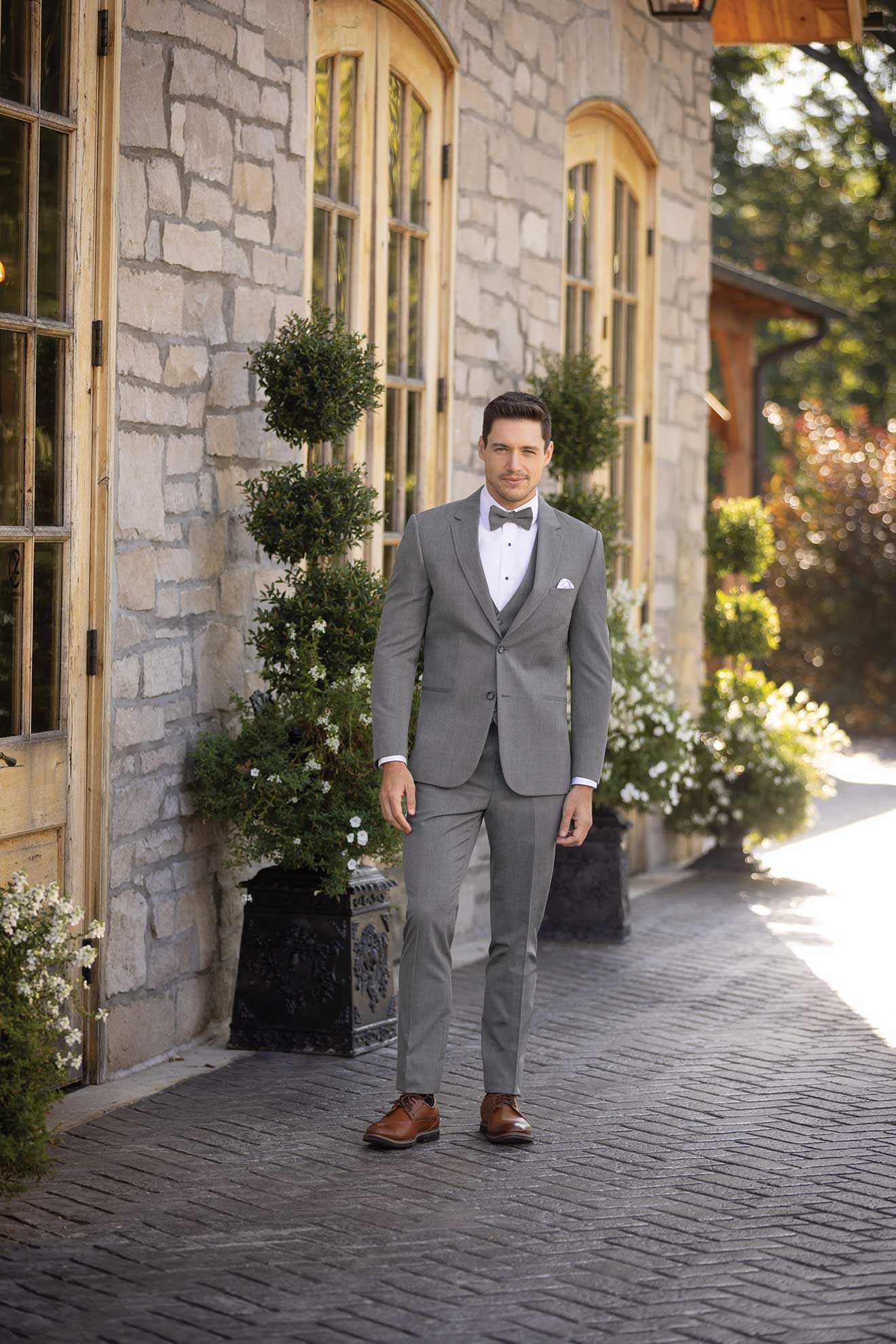 A man in a Michael Kors Medium Grey Performance standing in front of a building for tuxedo rental.