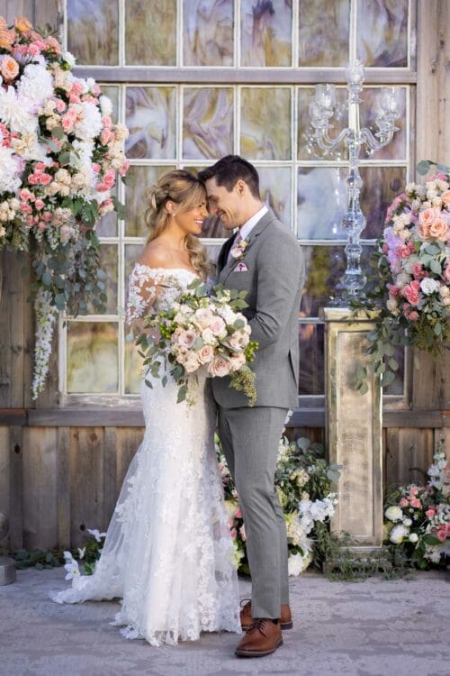 A bride and groom, dressed in elegant wedding attire, standing in front of a Michael Kors Medium Grey Performance.