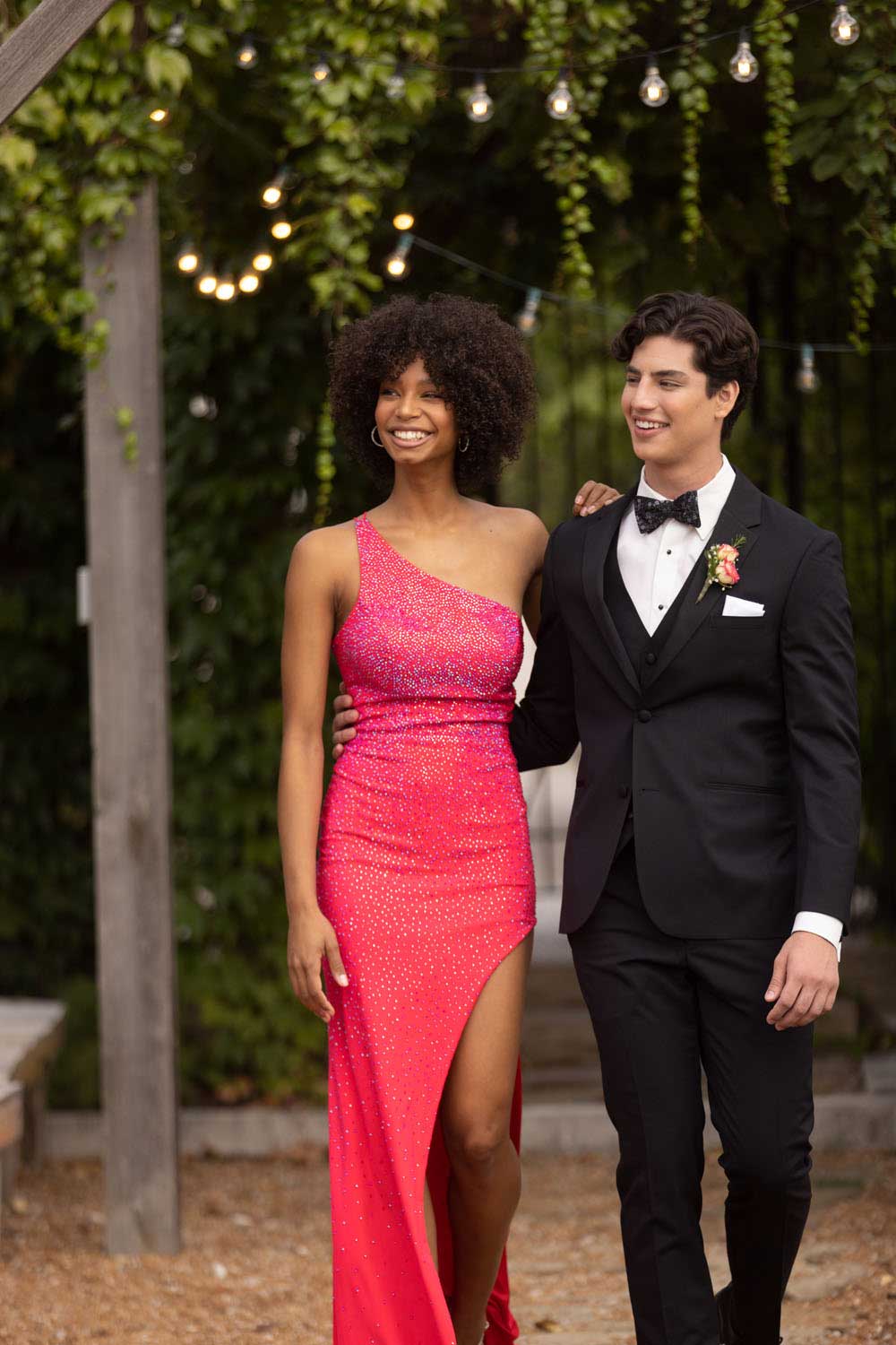 A man in a Michael Kors Black Performance tuxedo and woman in a red dress walking down a path.