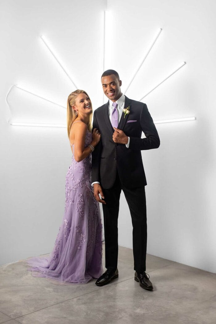 A man and woman, dressed in elegant attire from Michael Kors Berkeley, posing in front of a neon light.