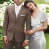 A man and woman, dressed impeccably in Ike Behar Brown Archer suits rented from the finest tuxedo rental service, strike a pose for a picture amidst the vibrant blooms of a garden.