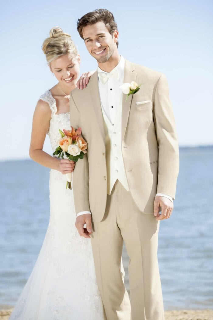 A bride and groom standing on the beach in Lord West Tan Havana tuxedos.