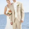 A bride and groom standing on the beach in Lord West Tan Havana tuxedos.