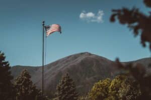 An american flag flies in front of a majestic mountain.