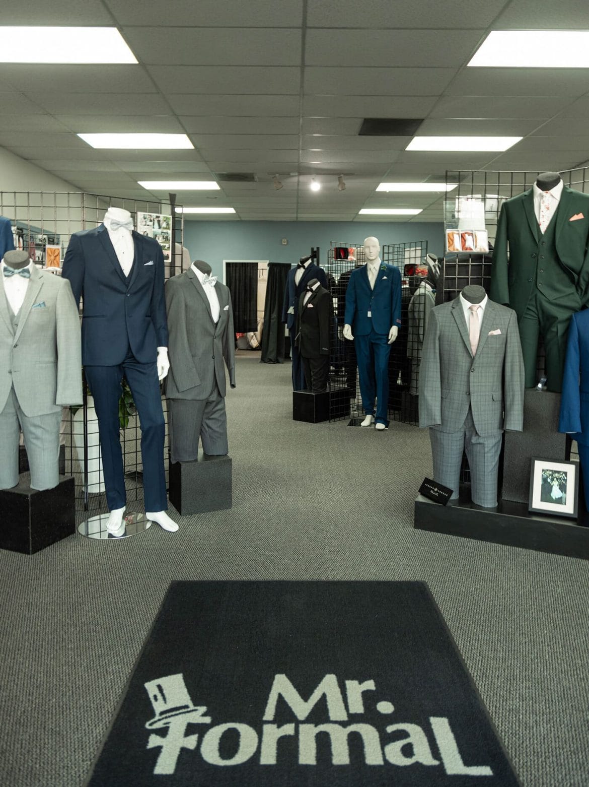Mannequins dressed in tuxedos for suit rental in a store.