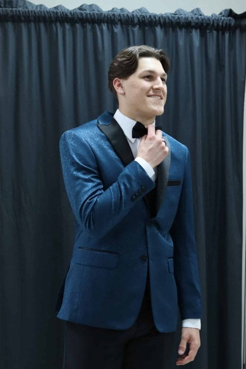 A young man in a Paisley Slim Fit Tuxedo rental standing in front of a curtain.