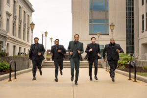 A group of men in suits running down a sidewalk.