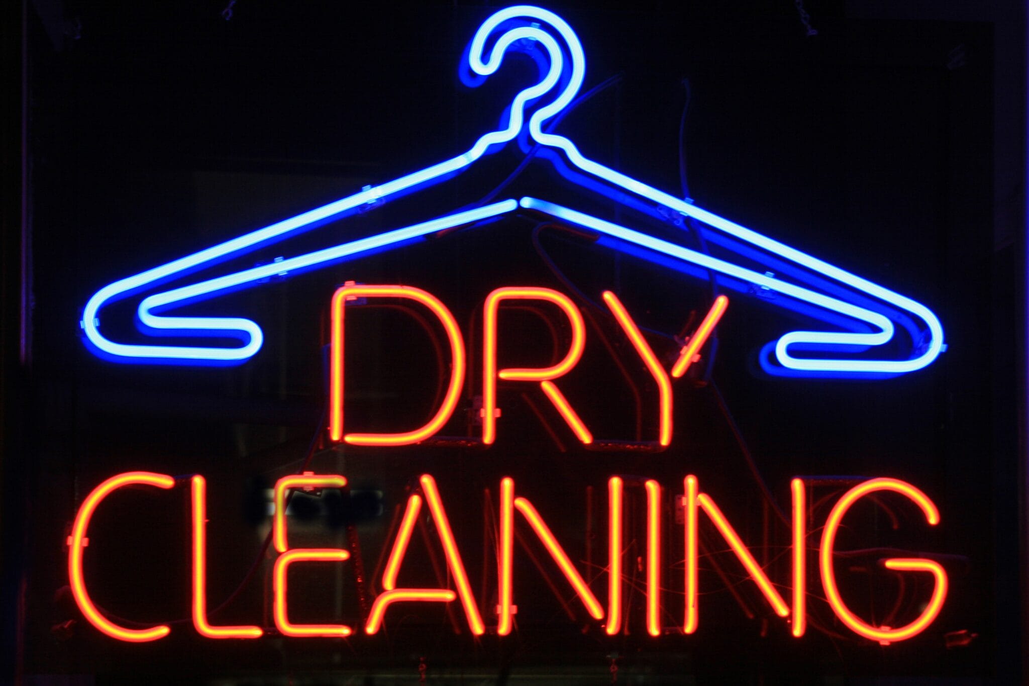 Neon sign with a blue hanger outline above red text that reads "DRY CLEANING.